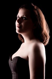 Portrait clair obscur d'une jeune fille rousse, de profil, portant un buster