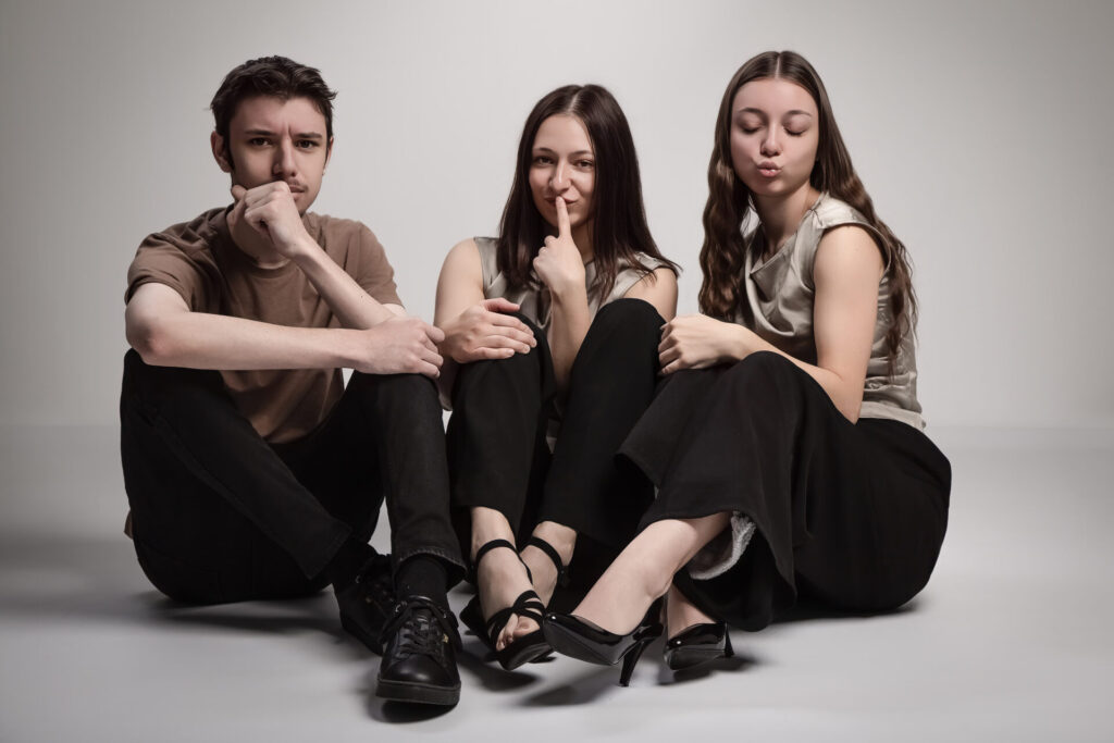 Photo décontractée des trois jeunes gens assis par terre ; ils font des grimaces et des gestes amusés (doigt sur la bouche, moue), Studio Salvucci, Photographe Metz