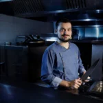 Jeune chef barbu dans une cuisine, tenant un grand couteau.