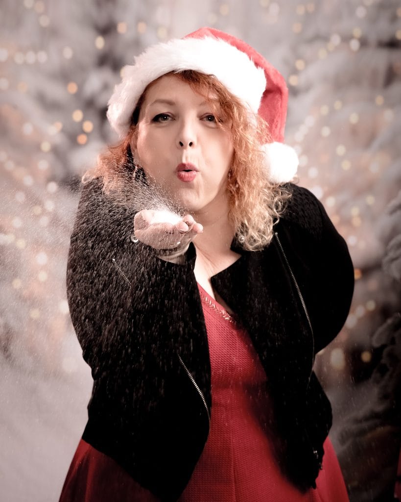 Femme joyeuse soufflant de la neige artificielle avec chapeau de Noël.