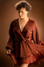 Femme aux cheveux bouclés, robe satinée rouille, maquillage jaune.