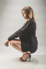 Femme blonde en blazer noir et talons, accroupie, fond gris photographiée par le Studio Salvucci à Metz.