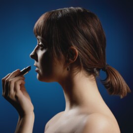 1er tableau du triptyque "Liberté Chérie" de l'objectif d'Or 2025 Portrait de profil d'une femme brune sur fond bleu profond, s'appliquant délicatement du rouge à lèvres foncé sous une lumière contrastée, par Aurélien Salvucci, Photographe du Studio Salvucci à Metz