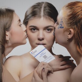 2ème tableau du triptyque "Liberté Chérie" de l'objectif d'Or 2025 Composition artistique de trois jeunes femmes sur fond gris : celle du centre tient une carte électorale française entre ses lèvres pendant que les deux autres l'embrassent sur les joues par Aurélien Salvucci, Photographe du Studio Salvucci à Metz