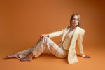 Femme en blazer jaune et pantalon dentelle assise sur fond orange photographiée par le Studio Salvucci à Metz