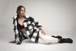 Portrait de studio par Studio Salvucci Metz : femme assise au sol en pose décontractée, chemise à carreaux noir et blanc oversize, legging blanc, bottines chunky noires, fond gris uni.