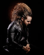 Homme aux cheveux longs, veste cuir noire, regard baissé, mains jointes photographié par le Studio Salvucci à Metz.