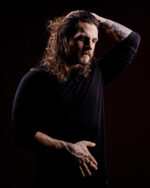 Homme barbu aux cheveux longs et bouclés, bras tatoué photographié par le Studio Salvucci à Metz.